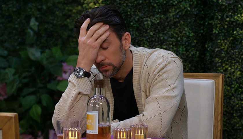 Y&R Scoop: Cane puts his hand over his face as he sits in front of a bottle