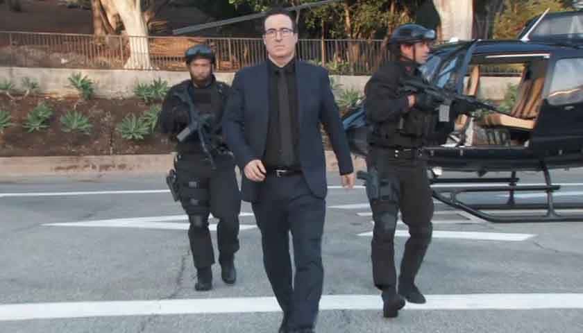 GH Scoop: John Oliver struts alongside two armed officers, in front of a helicopter