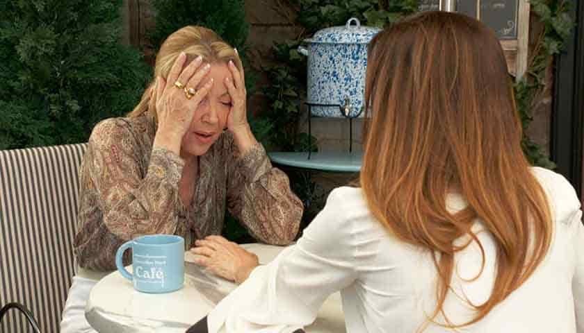 Y&R Scoop: Nikki clasps her head in pain as she sits at a table with Victoria