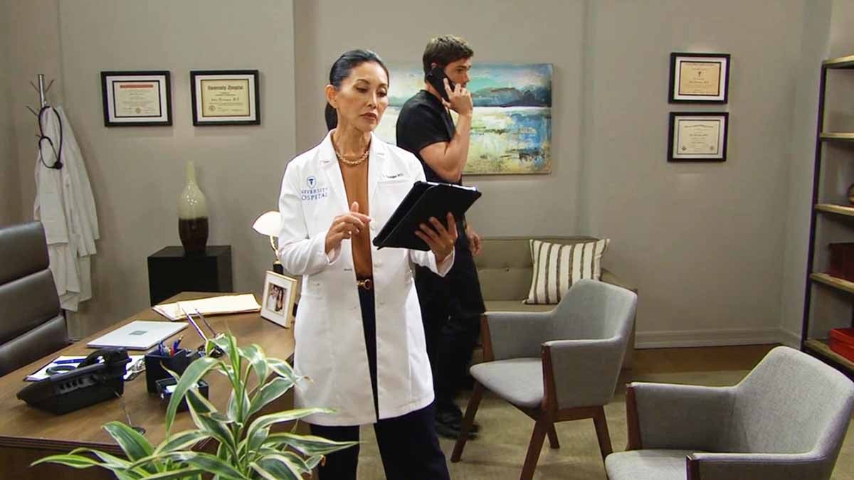 Li looks down at her tablet as Finn stands behind her on the phone on Bold and the Beautiful